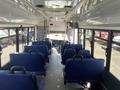 Interior view of a 2020 Chevrolet Express bus showing rows of blue seats and vehicle controls at the front
