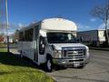 A white 2014 Ford Econoline bus with large windows and a high roof parked on the street