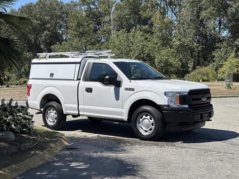 A white 2019 Ford F-150 is parked with a utility cap and a ladder rack on its roof, featuring a black grille and wheels
