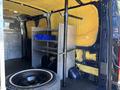 Interior of a 2016 Ford Transit 150 featuring yellow insulation on the walls a metal shelving unit and a spare tire on the floor