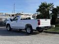 A white 2024 Chevrolet Silverado 1500 pickup truck with a standard cab and bed viewed from the rear showing its sleek design and logo on the tailgate