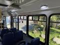 Interior view of a public transportation bus showing empty blue seats and multiple windows with sunlight coming through