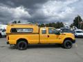 A yellow 2013 Ford F-250 SD with a camper shell is parked, featuring a black wheel design and a side profile view