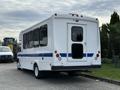 A white 2015 Chevrolet Express bus with a blue stripe and large rear door parked on a concrete surface