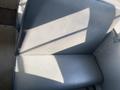 A grey bus seat from a 2006 Thomas Saf-T-Liner HDX with a smooth surface and visible sunlight casting shadows on it