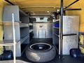 Interior of a 2016 Ford Transit 150 featuring metal shelves on both sides a central storage unit and a spare tire on the floor