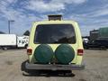 A yellow 1976 GMC Motorhome viewed from the rear featuring two green spare tire covers and chrome detailing on the bumper