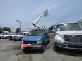 A blue 2005 Ford Econoline van with an orange traffic cone in front, parked next to a white truck, featuring a raised lift mechanism on its roof