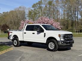 A 2021 Ford F-250 Super Duty pickup truck in white with a chrome grille and a bed cover parked on a street
