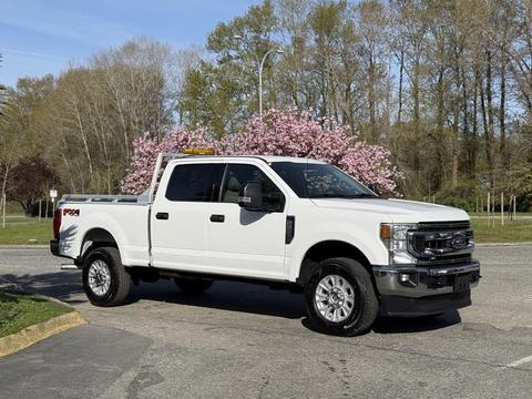 A 2021 Ford F-250 Super Duty pickup truck in white with a chrome grille and a bed cover parked on a street