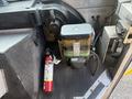 A 2012 Ford Econoline's interior featuring a black container with a green label and a red fire extinguisher positioned next to it on a textured floor mat
