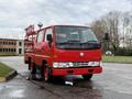 A red 2001 Toyota Dyna truck with a flatbed and a ladder rack on top parked on a road