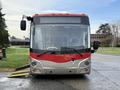 A 2016 Grande West Vicinity bus with a red and silver exterior is parked facing forward with its headlights on and windshield wipers visible