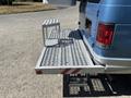 A blue 2008 Ford E-350 with a metal service platform attached to the back featuring a grated surface and a small support shelf
