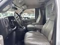 Interior view of a 2022 GMC Savana showing the driver's seat and passenger seat with a gray leather finish and a partition behind the front seats