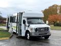 A 2009 Ford Econoline bus with a white exterior and green accents has the passenger door open and is parked on a roadway