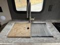 A modern kitchen sink area featuring a sleek faucet, a wooden cutting board, and a draining rack integrated with a marble countertop