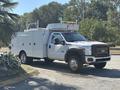 A white 2011 Ford F-550 with a utility body and a ladder rack on top parked with tools and equipment storage compartments on the sides