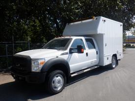 A white 2012 Ford F-550 with a large box-shaped cargo area mounted on the back and dual rear wheels