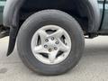 A close-up view of a silver alloy wheel with five spokes and a Michelin tire mounted on a green 2004 Toyota Tacoma