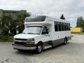 A white 2020 Chevrolet Express shuttle bus with large windows and a black stripe along the bottom parked on a concrete surface