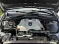 Close-up of the engine compartment of a 2004 BMW 6-Series featuring a silver engine cover with the BMW logo and various mechanical components