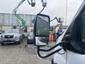 A 2021 Ford Transit-350 with a side mirror reflecting raindrops and a blurred background of vehicles and machinery