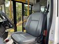 A gray driver seat inside a 2018 Ford Transit-350 with a view of the dashboard and entrance area