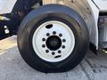 A close-up of a black tire mounted on a white wheel of a 2019 Freightliner M2 106 featuring multiple black lug nuts in the center