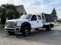 A 2015 Ford F-550 white truck with a flatbed and black toolboxes on the sides featuring a prominent grille and large wheels