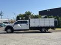 A white 2019 Ford F-550 with a flatbed and metal sides is parked with its profile facing the viewer