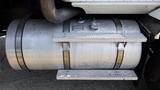 A silver fuel tank with a textured step attached to a large truck showing metallic surface and fittings