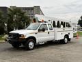 A white 2001 Ford F-350 truck with a bucket lift attached it has an extended cab and utility bed with storage compartments