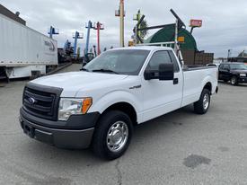 A white 2013 Ford F-150 pickup truck with a black grille and a flatbed in the rear parked at a facility