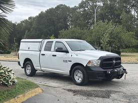 A white 2016 RAM 1500 truck with a cargo cap and front-mounted winch parked on a paved surface