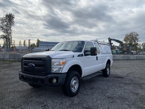 A white 2015 Ford F-250 Super Duty truck with a utility bed and black front grille parked on gravel