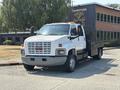 A 2005 GMC C7500 Topkick truck with a flatbed and side rails parked on a street with a white cab and grey accents