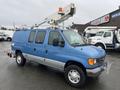 A blue 2006 Ford Econoline van with a bucket lift mounted on top and multiple windows on the side