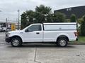 A 2020 Ford F-150 in white with a utility cap on the bed parked beside greenery and industrial structures