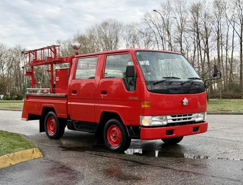 A red 2001 Toyota Dyna truck with a flatbed and a ladder rack on top parked on the pavement