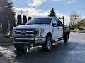 A white 2020 Ford F-350 truck is parked with a flatbed attachment showcasing its robust design and large wheels