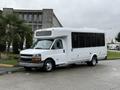 A 2013 Chevrolet Express bus with a white exterior and large windows parked on a concrete surface