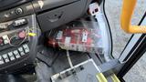 A red mechanical device housed in a transparent casing, located on the floor of a 2021 Ford Transit vehicle near the driver's seat