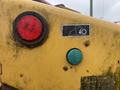 Close-up of a yellow Vermeer Corporation BC1000XL with a red taillight a green control button and machinery indicator symbol on a worn surface