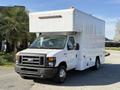 A 2012 Ford Econoline E-450 with a boxy white cargo body and a flat front grille parked on a road