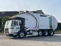 A 2011 Autocar Xpeditor garbage truck with a white body and green stripes on the side parked with its compaction mechanism visible