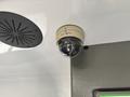A security camera mounted on a ceiling with a spherical lens and the brand name SEON visible on its casing