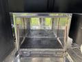 An empty stainless steel storage compartment with a textured black floor grid and metal bars on the sides inside a 2013 Freightliner 114SD