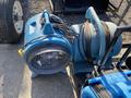 A blue industrial air mover with a circular fan and attached power cord, positioned next to other similar equipment in a restoration lot