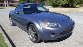 A 2007 Mazda Miata in a metallic gray color parked with the top up displaying sleek lines and sporty wheels